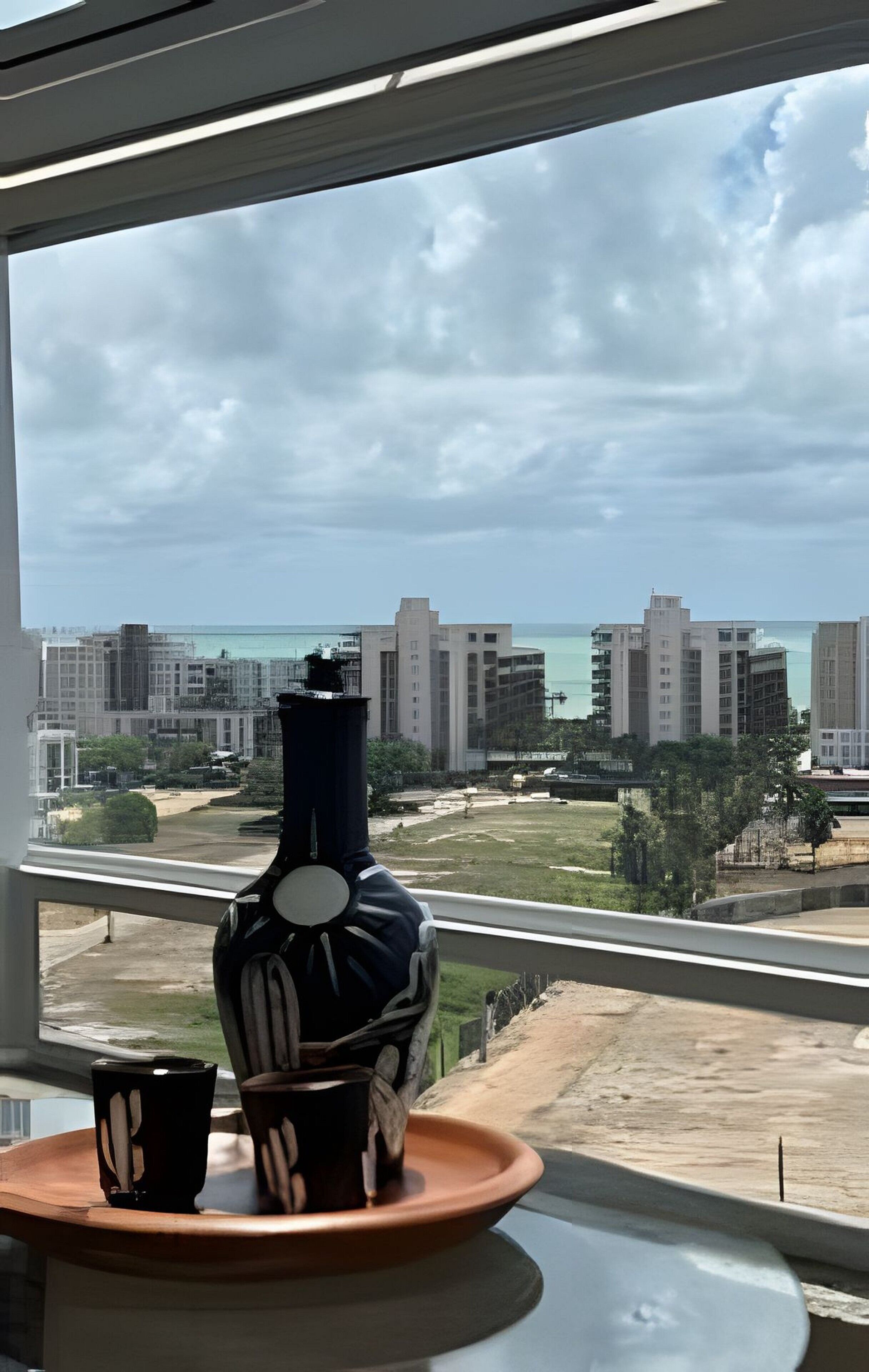 Une vue depuis une fenêtre donnant sur un paysage urbain, avec des bâtiments et une étendue d’eau.