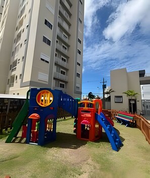 A playground with slides and climbing structures, surrounded by residential buildings. - 2 Qtos I Praia I Lazer  I João Pessoa (Cabedelo)
