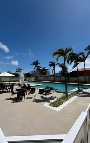 A pool area with lounge chairs and umbrellas, surrounded by palm trees and a clear sky. - 2 Qtos I Praia I Lazer  I João Pessoa (Cabedelo)