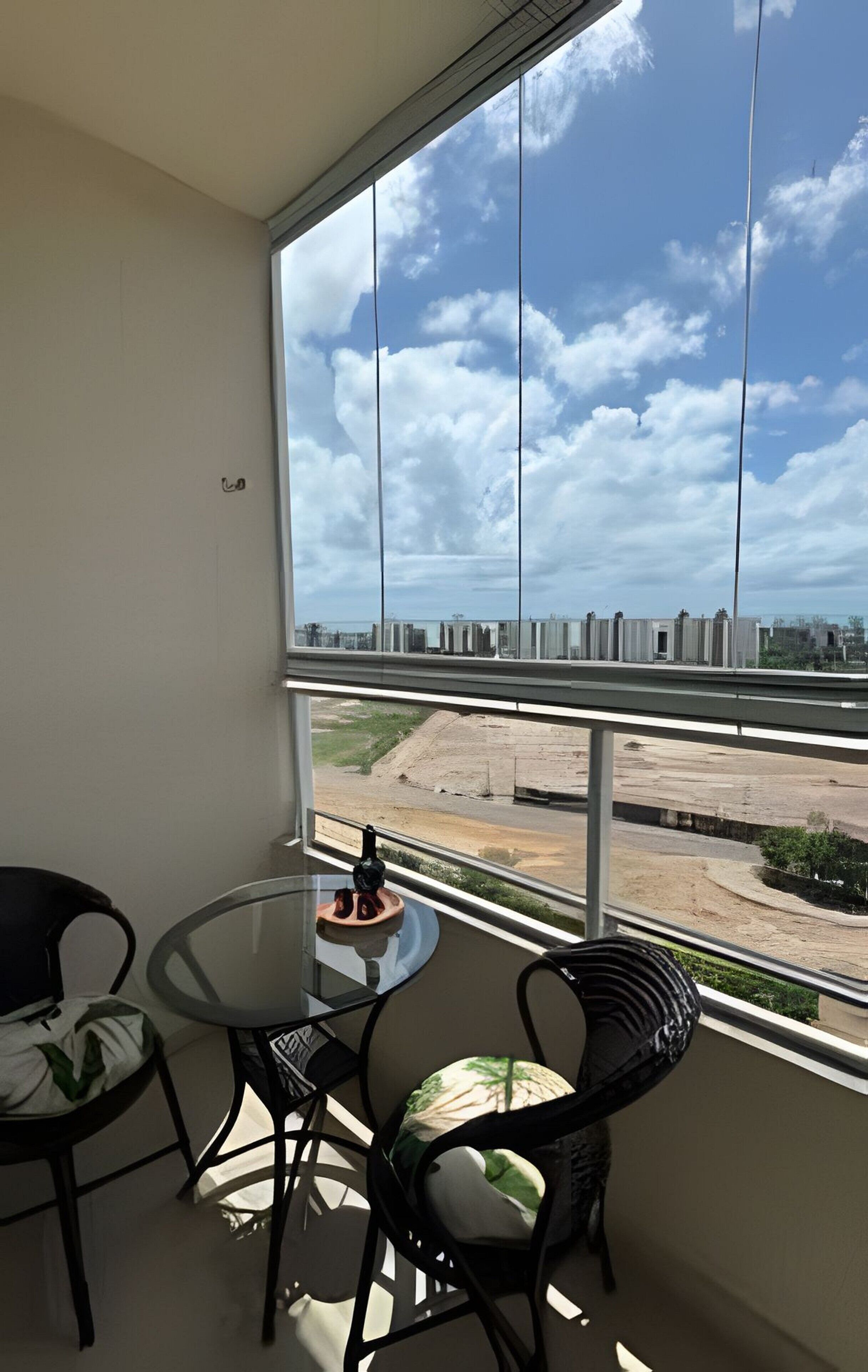 A balcony with a glass table and chairs, overlooking a construction site and buildings.