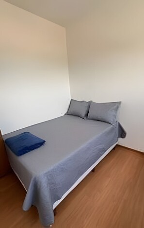 A single bed with a grey mattress and pillows, a blue blanket, and a wooden floor. - 2 Qtos I Praia I Lazer  I João Pessoa (Cabedelo)