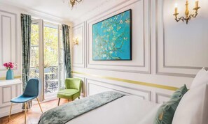 A hotel room with a bed, a green chair, a blue chair, a painting on the wall, and a window with curtains. -  A COMBINATION OF A CLASSIC PARISIAN ARCHITECTURE WITH MODERN COMFORT (Paris)