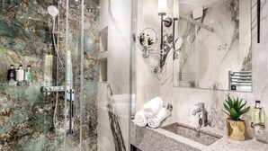 Bany modern amb dutxa tancada per vidre, parets de marbre, un lavabo amb mirall i productes de tocador.