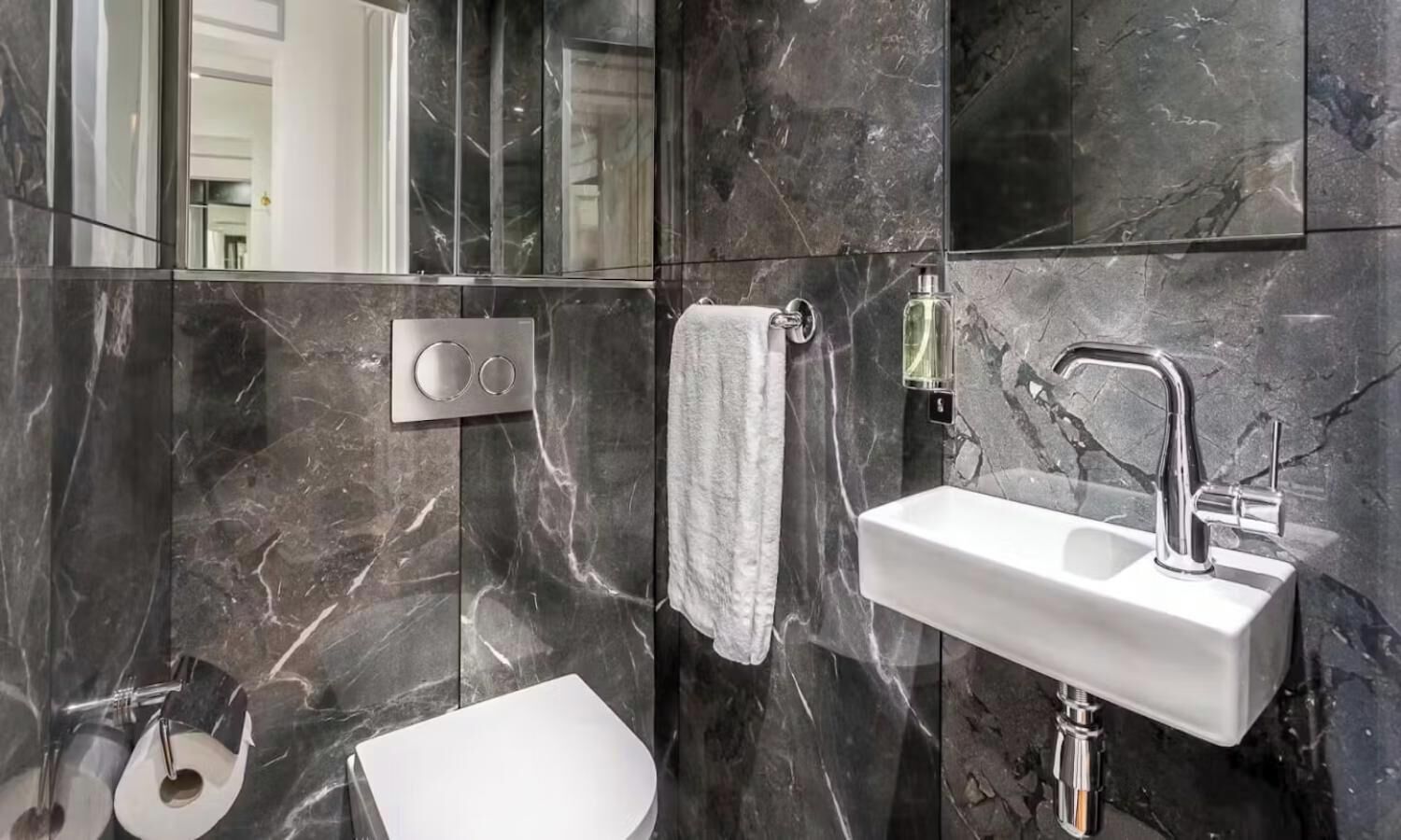 Ein modernes Badezimmer mit einem weißen Waschbecken, einem Handtuch auf einem Halter und einer Toilette.