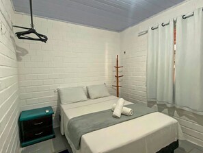 Quarto com cama, cabides, porta-roupas de madeira e janela com cortinas.