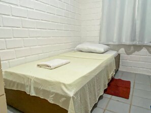 Quarto pequeno com uma cama de solteiro, parede de tijolos brancos, colcha branca, travesseiro branco e um tapete vermelho.