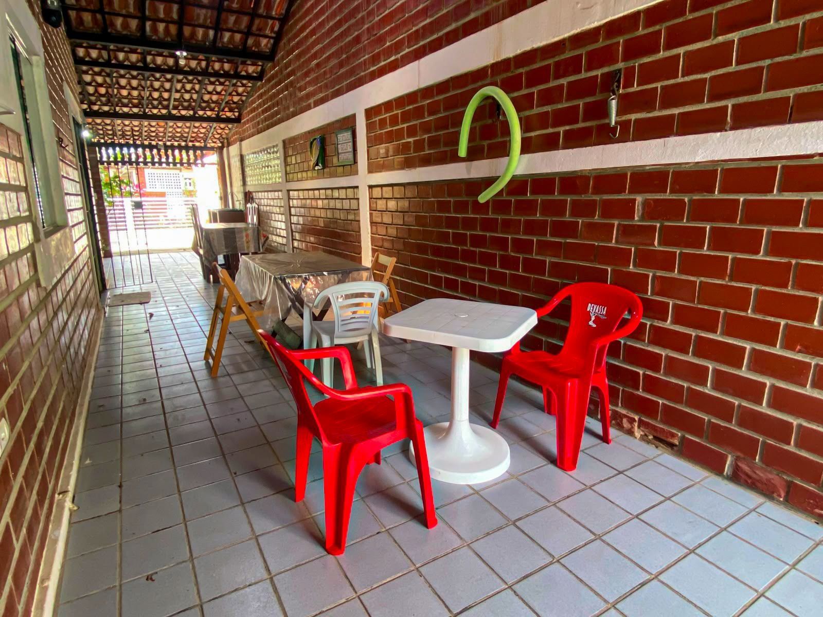 Uma área de estar coberta ao ar livre, com paredes de tijolo, piso de azulejo e cadeiras de plástico vermelho.