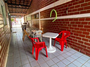 Uma área de estar coberta ao ar livre, com paredes de tijolo, piso de azulejo e cadeiras de plástico vermelho.