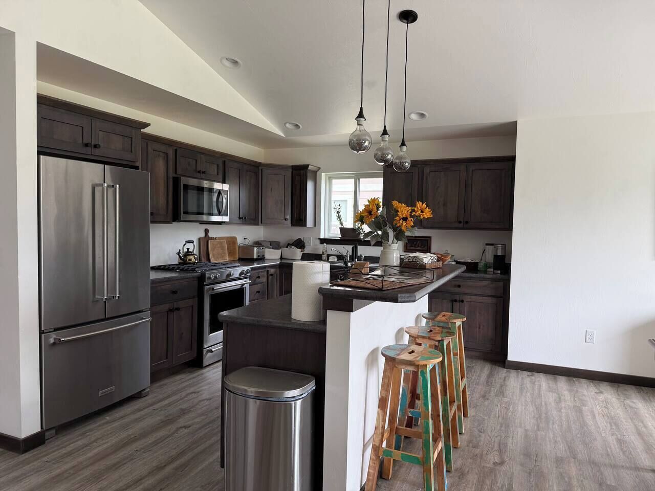 A modern kitchen with dark wood cabinets, stainless steel appliances, and a central island with stools.