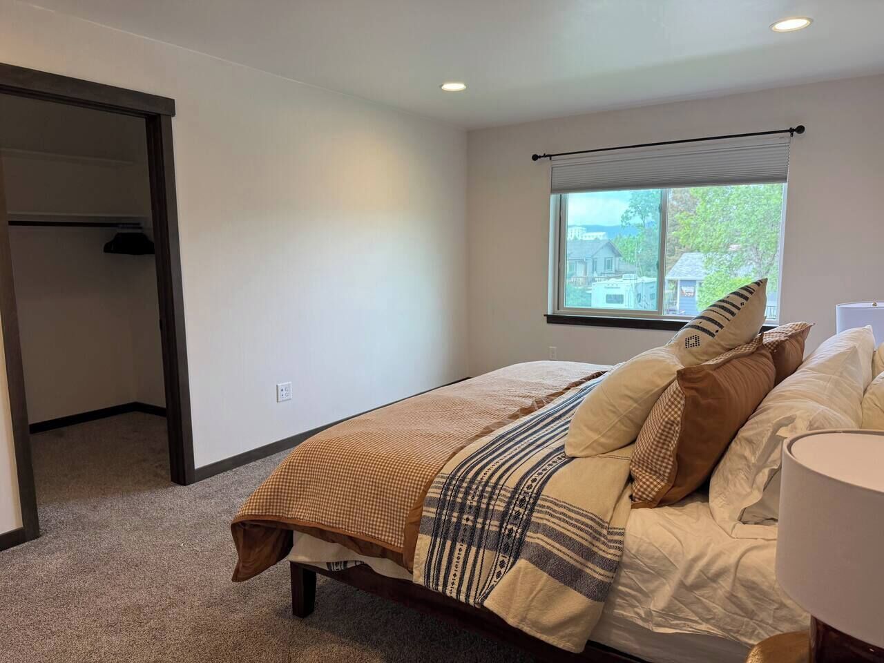 A bedroom with a bed, a window, a door, and a lamp.