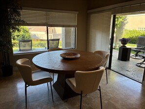 A dining area with a round table, six chairs, and a large window with blinds. - 2.5-bedroom house in lovely Palm Desert with AC (Palm Desert)