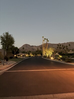 A well-lit street with a mountain in the background, surrounded by landscaped areas with trees and shrubs. - 2.5-bedroom house in lovely Palm Desert with AC (Palm Desert)