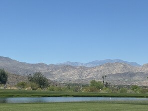 A landscape with a body of water, green fields, and mountains in the background. - 2.5-bedroom house in lovely Palm Desert with AC (Palm Desert)