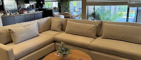 A modern living room with a sectional sofa, a coffee table, and a kitchen in the background.