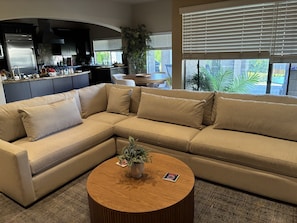 A modern living room with a sectional sofa, a coffee table, and a kitchen in the background. - 2.5-bedroom house in lovely Palm Desert with AC (Palm Desert)