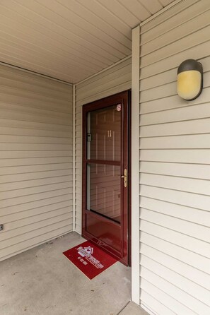 A closed wooden door with a glass panel, a doormat with a logo, and a wall-mounted light fixture. - Spacious Condo, Hot Tub, Sauna, Indoor  and Outdoor Pool Access! | C-11 (Branson)