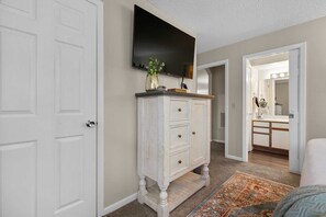 A hallway with a white door, a white dresser with drawers, a flat-screen TV mounted above it, and a bathroom visible through an open door. - Spacious Condo, Hot Tub, Sauna, Indoor  and Outdoor Pool Access! | C-11 (Branson)