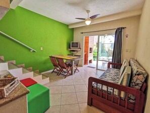 A living area with a green wall, a dining table with chairs, a sofa, a television, and a staircase. - COSTA ALLEGRA INGLESES RESIDENCE (Florianópolis)
