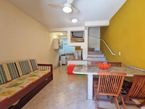 Una sala de estar con un sofá, una mesa de comedor con sillas, una escalera y una zona de cocina.