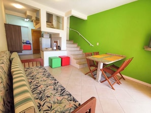 Una sala de estar con un sofá, una mesa de comedor con sillas, una escalera y una pared verde.