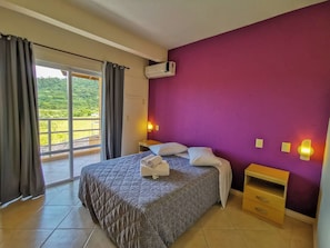 Un dormitorio con cama, mesita de noche, aire acondicionado instalado en la pared y vistas a través de una puerta corrediza de vidrio.