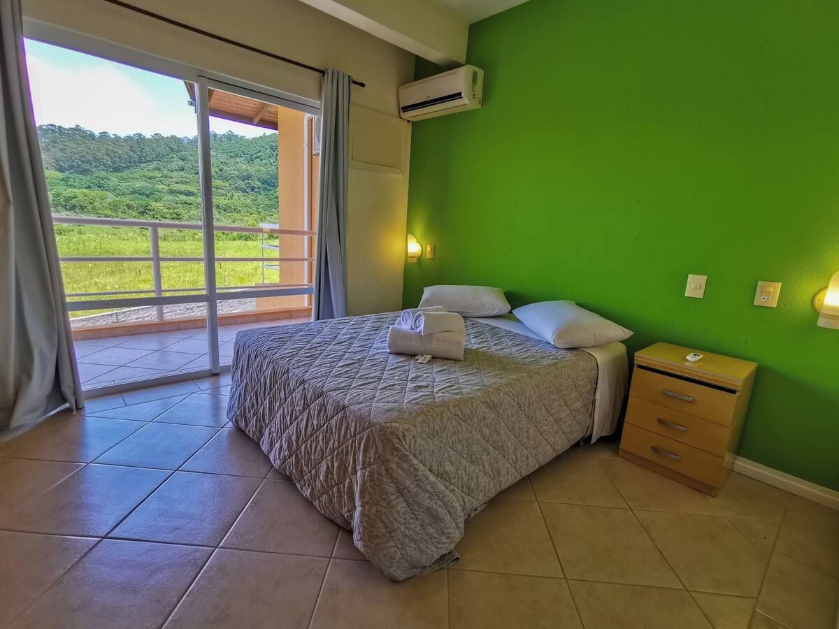 Een slaapkamer met een bed, een nachtkastje, een raam met uitzicht op groen en een airconditioning.