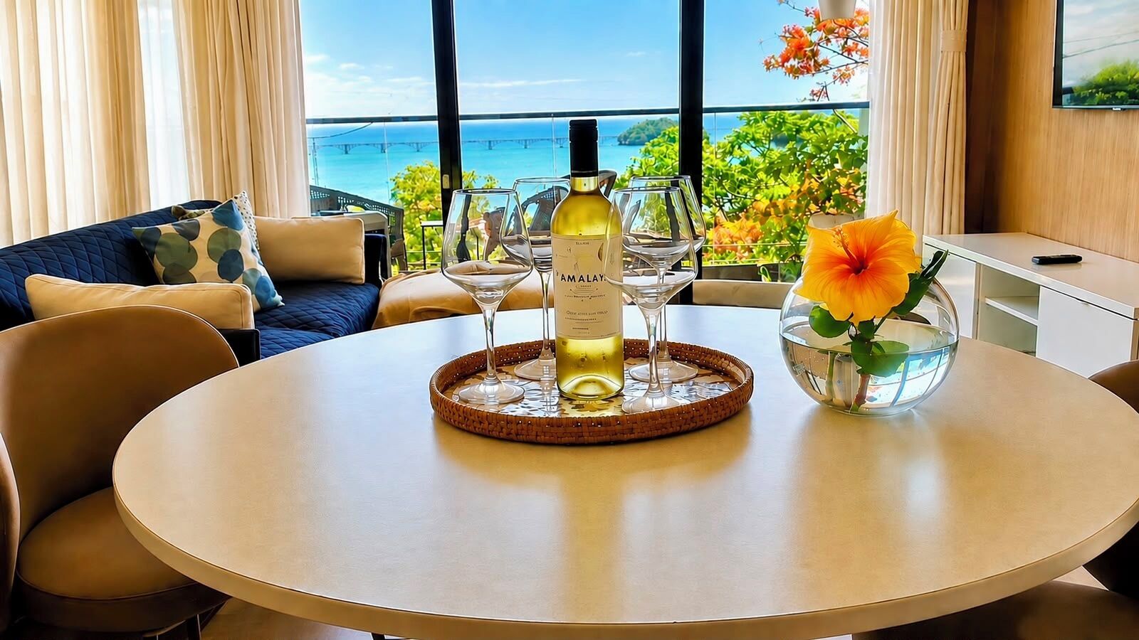 Une table ronde avec une bouteille de vin Amalay, deux verres à vin, un plateau en osier et un vase de fleurs.