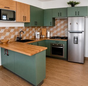 A kitchen with green cabinets, a stainless steel refrigerator, a microwave, and a wooden countertop. - LEVEL 2, Lovely 2-bedroom apartment with AC steps to malecon in Santa Barbara (Santa Barbara)