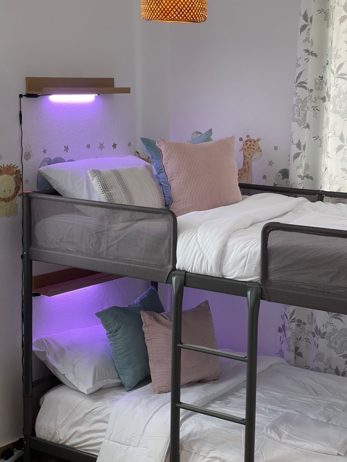 Uma cama beliche com cabeceira em tela, roupa de cama branca e uma luz roxa.