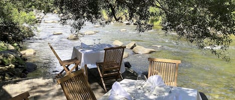 Ein Essbereich im Freien mit einem Tisch für sechs Personen, umgeben von Stühlen und Blick auf einen Fluss.