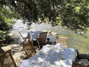 Un espace de restauration en plein air avec une table dressée pour six personnes, entourée de chaises, donnant sur une rivière aux eaux vives.