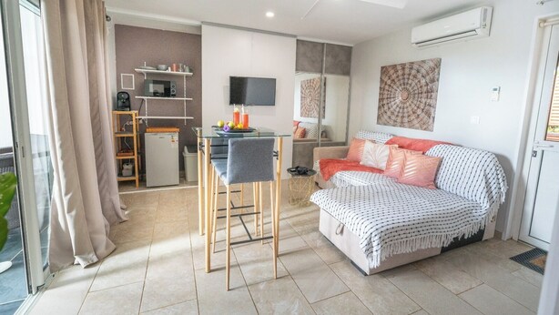 A modern living room with a sofa, a dining area with a glass table, and a kitchen area with a microwave. - Ti Kaz Romance, calm and relaxation (Sainte-Suzanne)