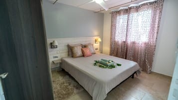 A bedroom with a bed, a nightstand, a ceiling fan, and a window with curtains.