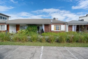 Una hilera de casas de un piso con techo plano, un pequeño jardín delantero y cielo despejado.