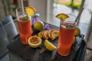 Two tall glasses of a red beverage with garnishes, placed on a dark tray with sliced fruits and a lime.