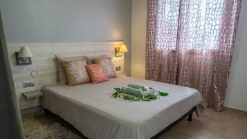A bedroom with a bed, a ceiling fan, a nightstand, a lamp, and a window with curtains.