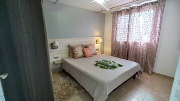 Une chambre à coucher avec un lit, une table de chevet, un ventilateur de plafond et une fenêtre avec des rideaux.