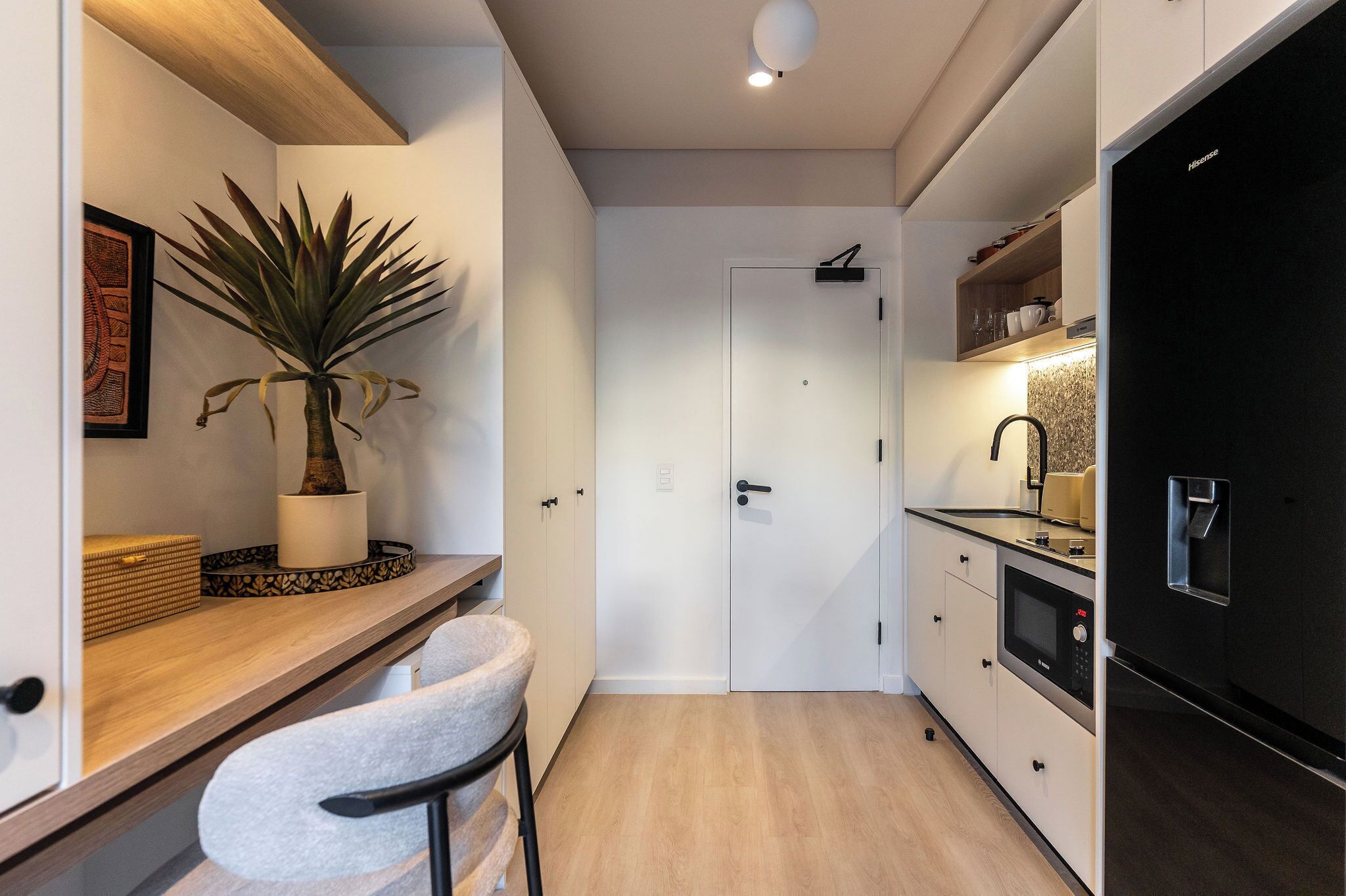 Une cuisine de taille réduite, avec un plan de travail en bois, une plante en pot, une porte blanche et un réfrigérateur noir.