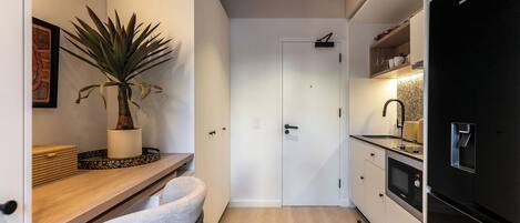 A compact kitchen with a wooden countertop, a potted plant, a white door, and a black refrigerator.