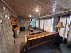 Ein gemütliches Zimmer mit Holzbalkendecke, einem Fernseher, einer Couch und Vorhängen.