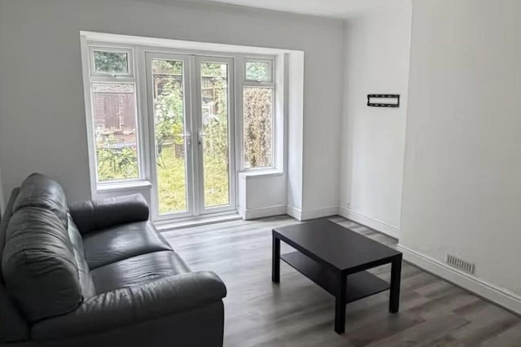 A room with a dark leather sofa, a small dark table, and a large sliding glass door leading to a garden.