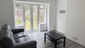 Habitació amb un sofà de cuir fosc, una taula petita fosca i una gran porta corredissa de vidre que dona a un jardí.