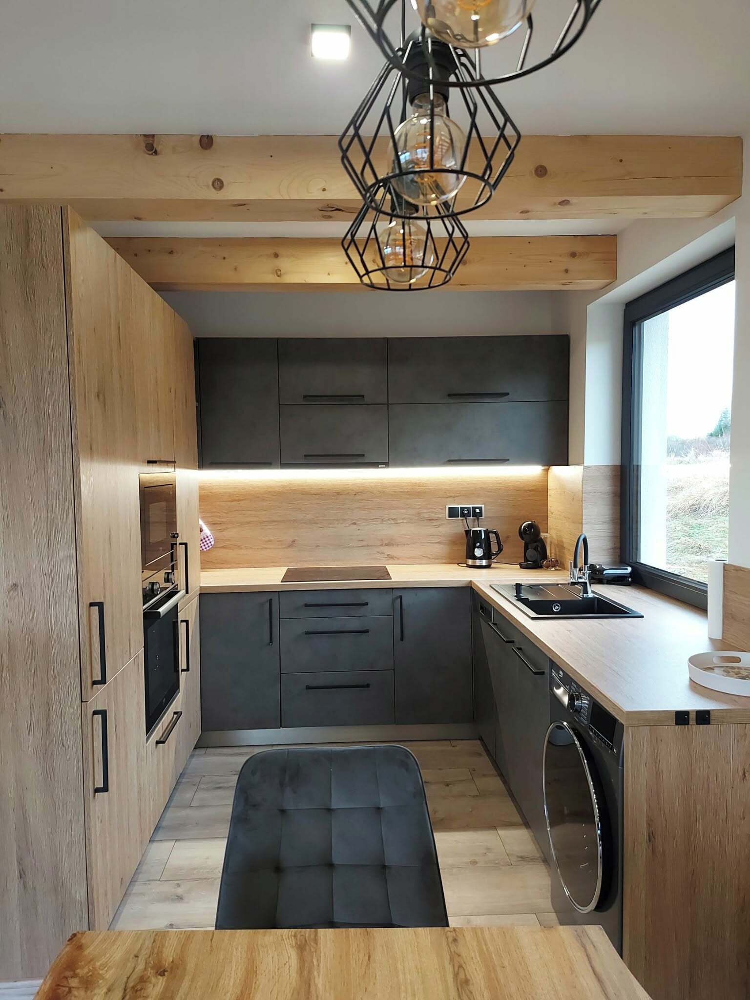 Une cuisine moderne avec des meubles en bois, un plan de travail noir et un four encastré.