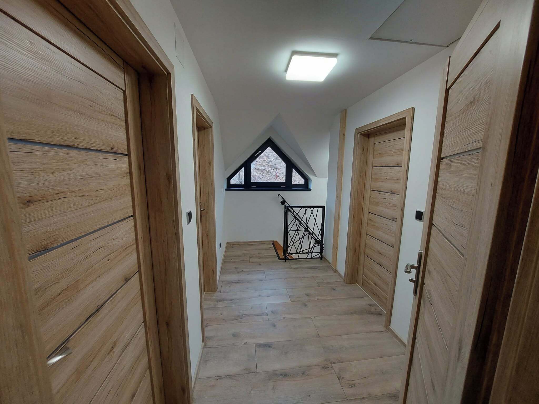 A hallway with wooden doors and a sloped ceiling with a skylight.