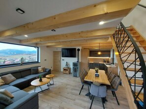 A modern living space with a wooden ceiling, a dining area, a sofa, a TV, and a staircase.
