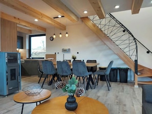 A modern interior with a dining area, kitchen, and a wooden staircase.