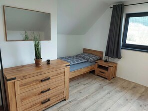 A bedroom with a bed, a wooden dresser, a nightstand, a mirror, and a window with curtains.
