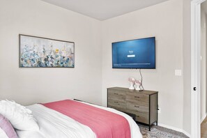 Un dormitori amb un llit, una petita taula de nit, un quadre i un televisor penjat a la paret.