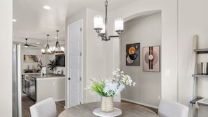A modern dining area with a round table, chairs, a vase of flowers, and a kitchen in the background. - Melon Ridge Getaway/King Suite/TVs in all rooms (Rio Rancho)