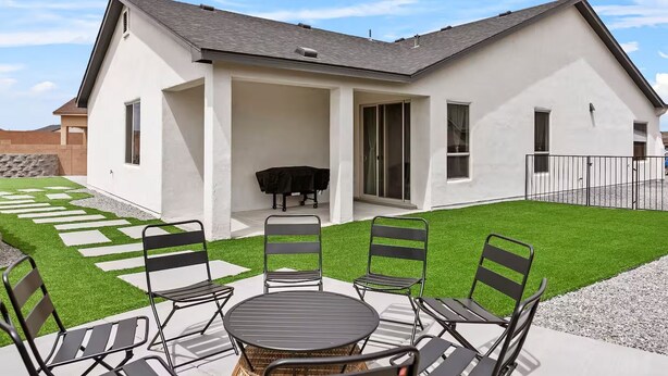 A modern house with a patio area featuring a round table and chairs, a barbecue grill, and a well-maintained lawn. - Melon Ridge Getaway/King Suite/TVs in all rooms (Rio Rancho)
